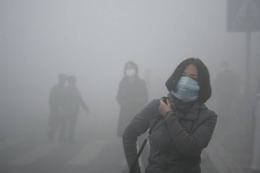 A woman wearing a mask walk through a street covered by dense smog in Harbin, northern China. Credit: Kyodo News